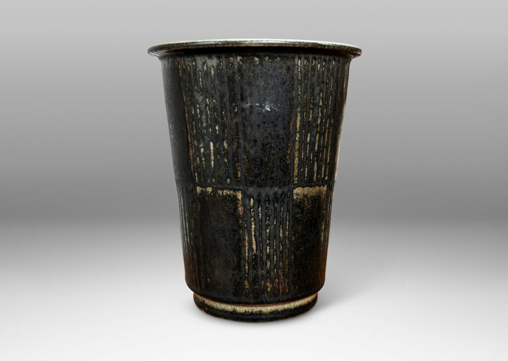 Gallery BAC wide tapered cylindrical form with alternating panels of carved verticals, glazed in brown-black with red luster