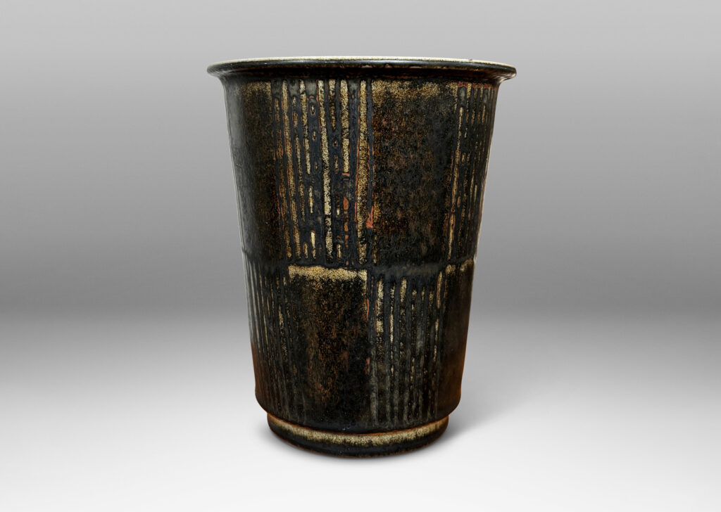 Gallery BAC wide tapered cylindrical form with alternating panels of carved verticals, glazed in brown-black with red luster