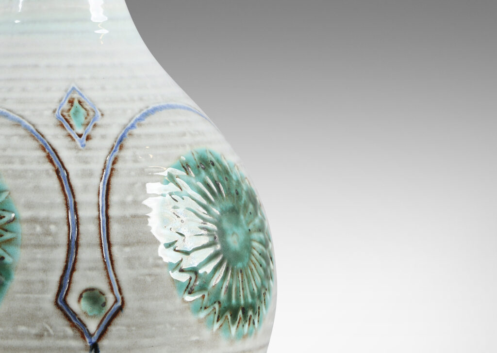 Gallery BAC globe form with tall sprouting neck, decorated with turning ridges and carved geometric folk-style ornaments, glazed in a pale gray-off white, with purple and green accent