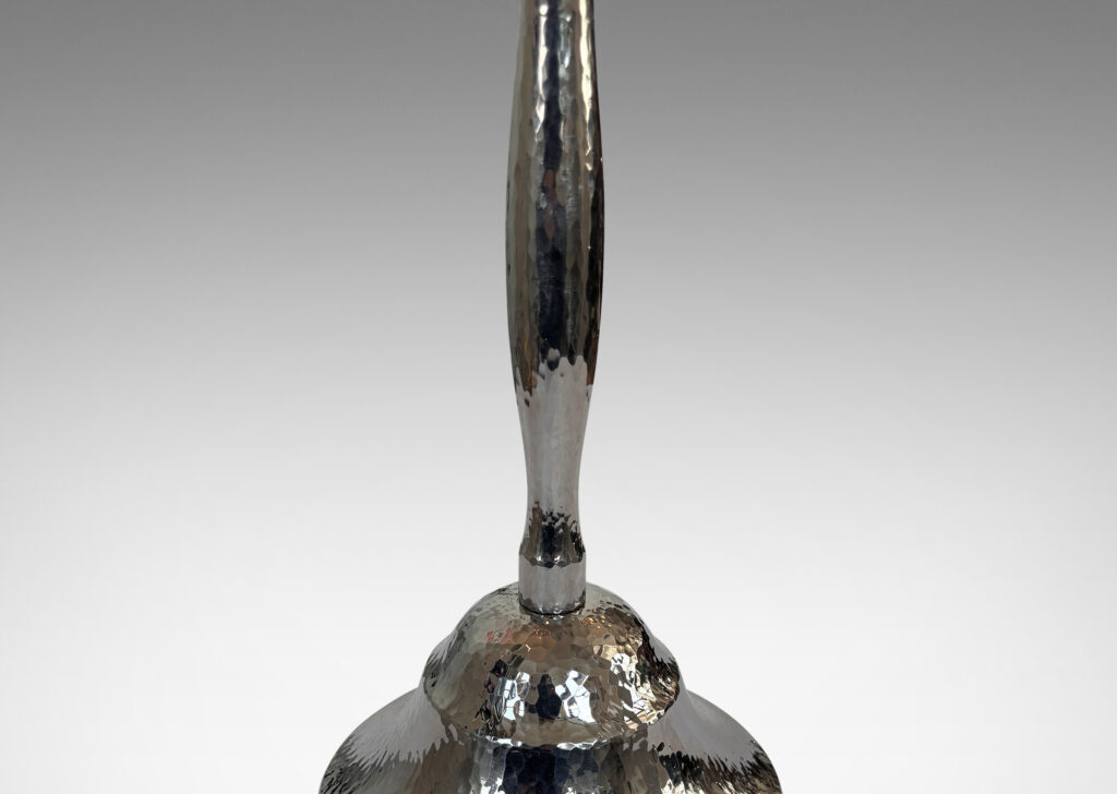Gallery BAC swelling stand on a bell-form base, finished in a hammered texture; polished steel