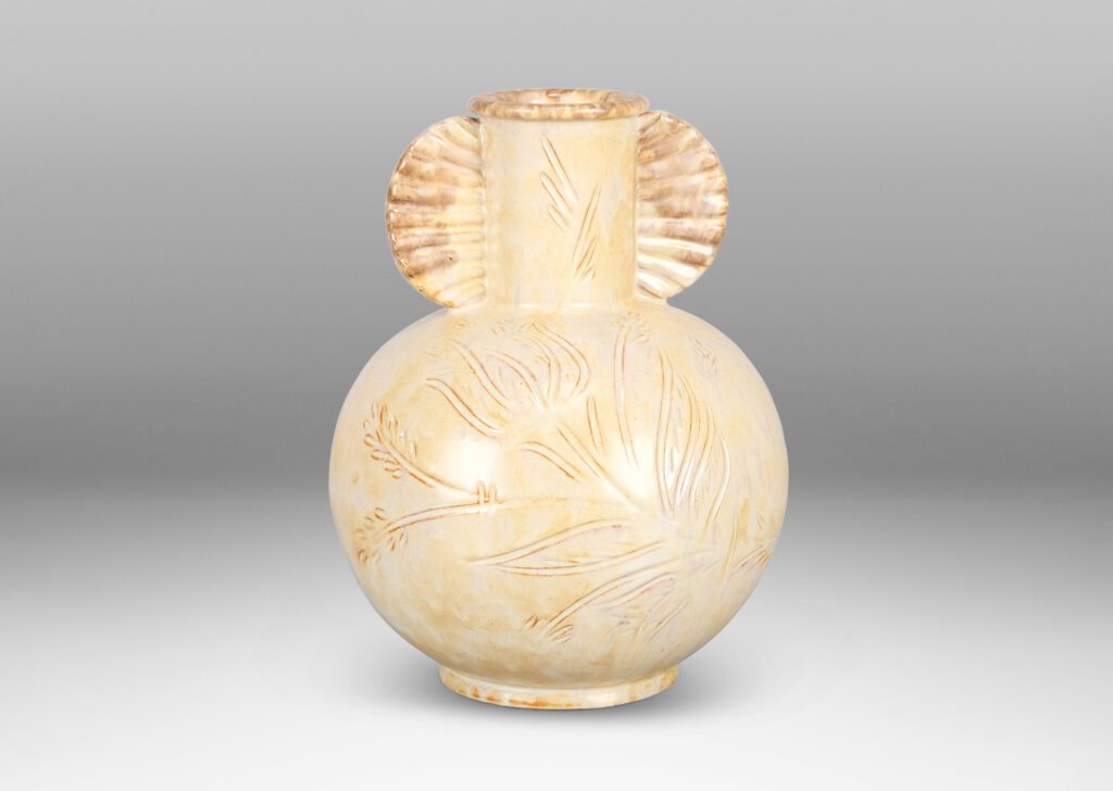 Gallery BAC globe form, with carved floral design, and neck framed by frill handles, glazed in sponged pale yellow-tan with hints of gray