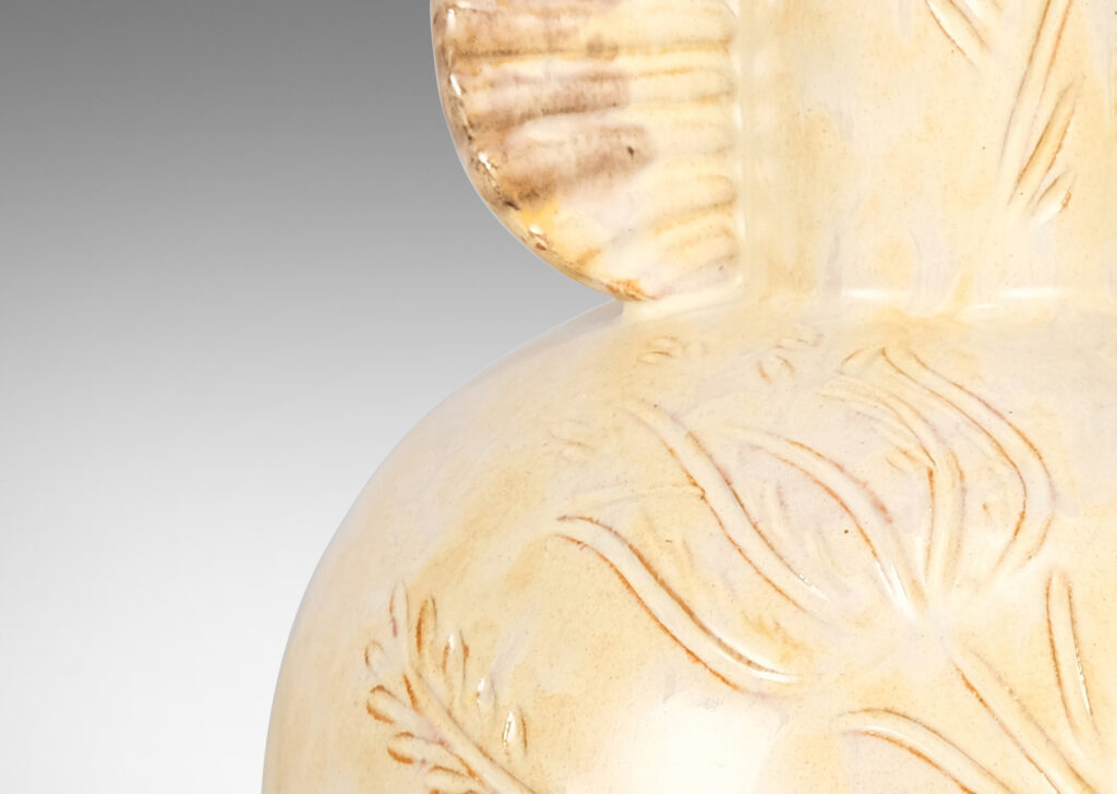 Gallery BAC globe form, with carved floral design, and neck framed by frill handles, glazed in sponged pale yellow-tan with hints of gray