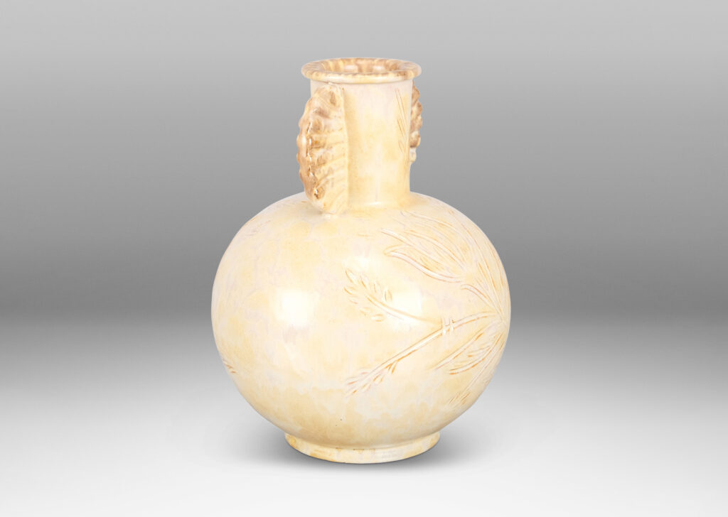 Gallery BAC globe form, with carved floral design, and neck framed by frill handles, glazed in sponged pale yellow-tan with hints of gray