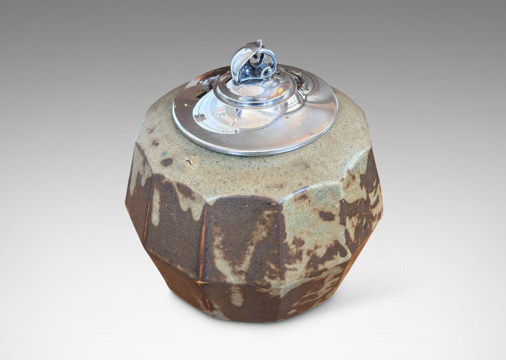 Gallery BAC angled and faceted form glazed in pale taupe-brown, with silver plated lid topped by a foliate finial