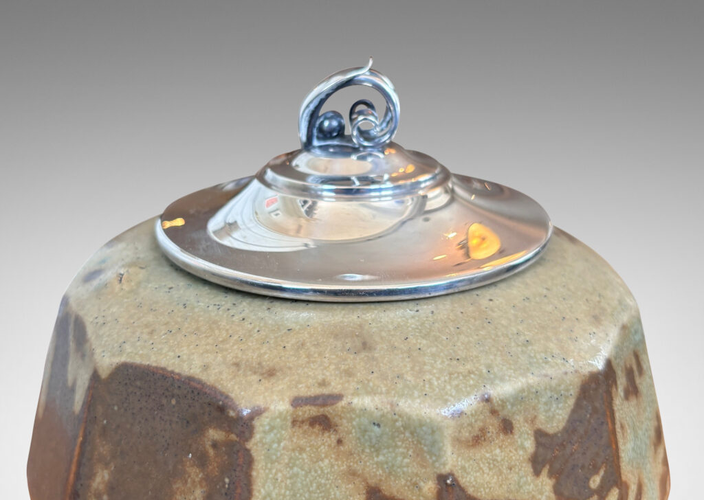 Gallery BAC angled and faceted form glazed in pale taupe-brown, with silver plated lid topped by a foliate finial