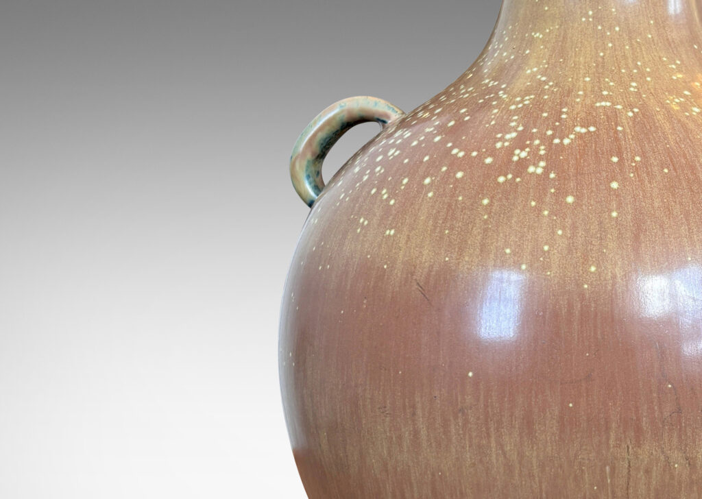 Gallery BAC globe form with sprouting neck and pair of ear-form handles, glazed in a flowing burnt sienna-ochre tan with pale speckling on shoulders