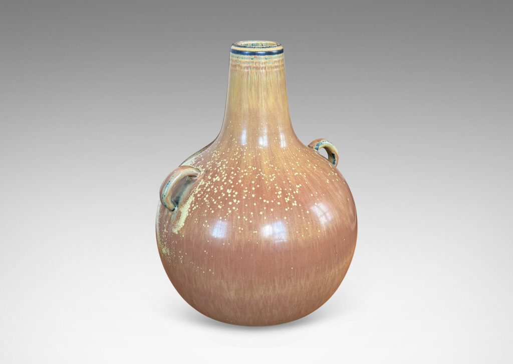 Gallery BAC globe form with sprouting neck and pair of ear-form handles, glazed in a flowing burnt sienna-ochre tan with pale speckling on shoulders