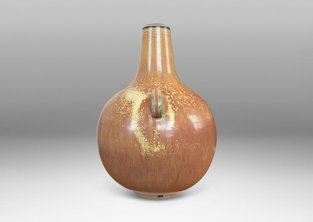 Gallery BAC globe form with sprouting neck and pair of ear-form handles, glazed in a flowing burnt sienna-ochre tan with pale speckling on shoulders