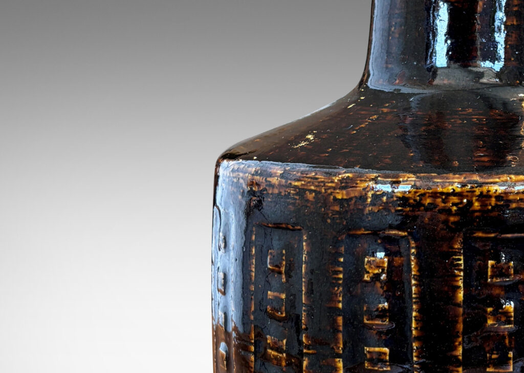 Gallery BAC low drum form with carved geometric design and tall neck, glazed in a dark brown