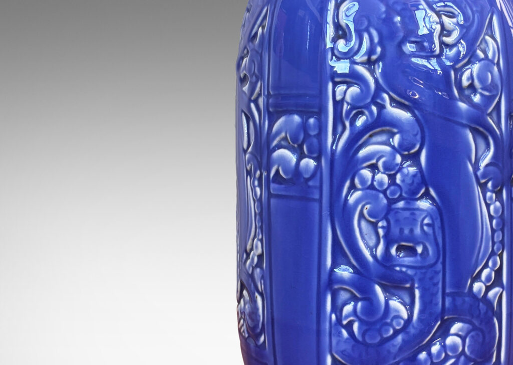 Gallery BAC upright ovoid form with flared mouth and relief panels depicting female figures, serpents and scrolling forms, glazed in dark cornflower blue