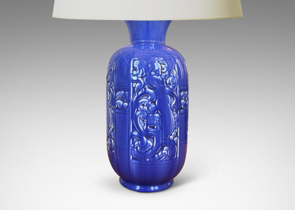 Gallery BAC upright ovoid form with flared mouth and relief panels depicting female figures, serpents and scrolling forms, glazed in dark cornflower blue