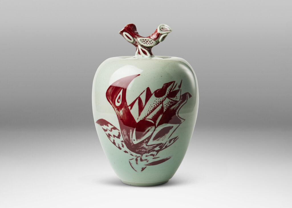 Gallery BAC tapered form and lid with branch-like finial, glazed in celadon with hand-painted abstracted fish, plants, shells and patterning in oxblood