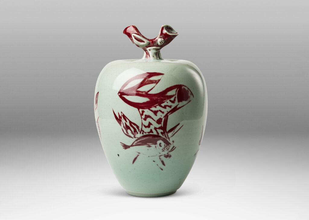 Gallery BAC tapered form and lid with branch-like finial, glazed in celadon with hand-painted abstracted fish, plants, shells and patterning in oxblood