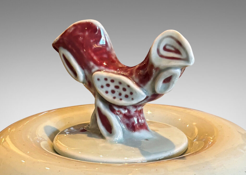 Gallery BAC tapered form and lid with branch-like finial, glazed in celadon with hand-painted abstracted fish, plants, shells and patterning in oxblood