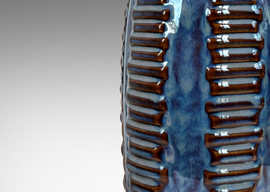 Gallery BAC swelling cylindrical forms ornamented with columns of relief bars, glazed in luster blue and matte brown