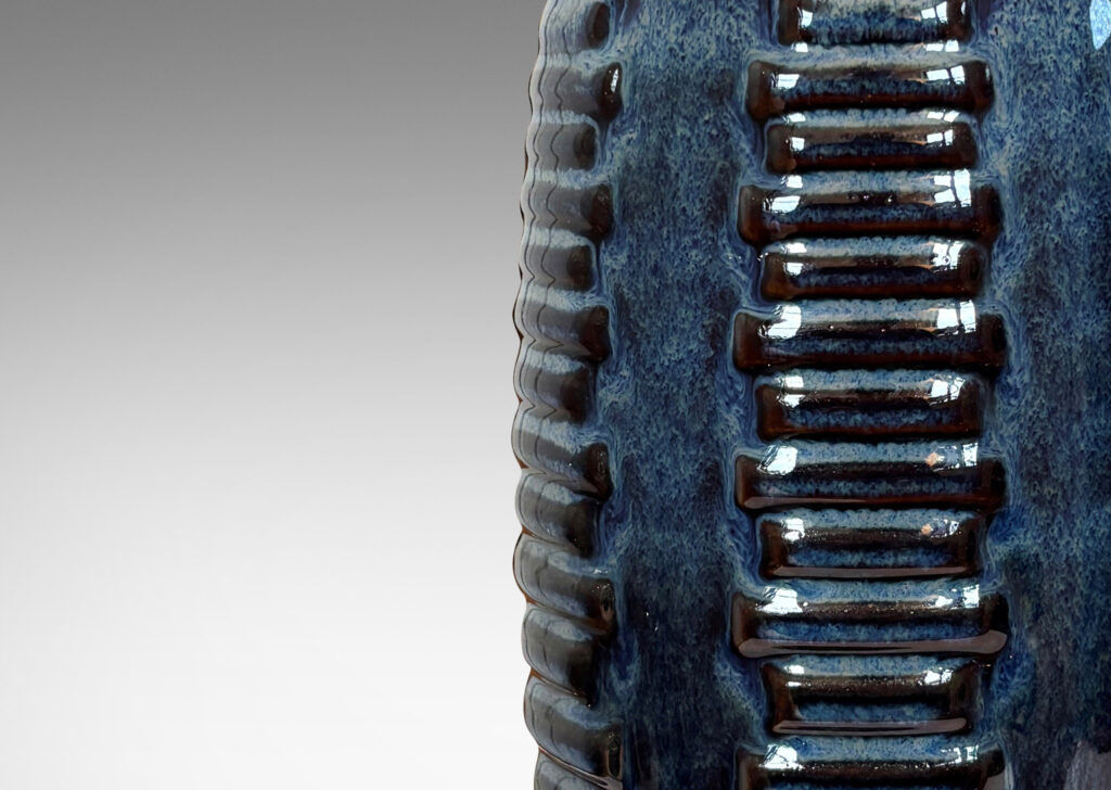 Gallery BAC swelling cylindrical forms ornamented with columns of relief bars, glazed in luster blue and matte brown