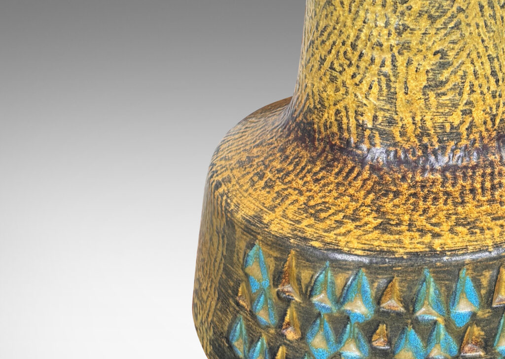 Gallery BAC floating drum form with wide conical neck, covered in a carved texture and ornamented with triangle motifs, and glazed in a mustard gold tone, with dark gray and turquoise elements