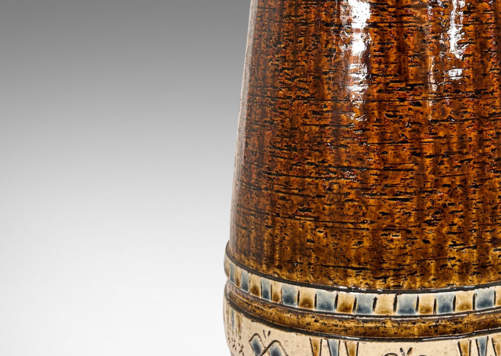 Gallery BAC having grog-textured ovoid cylindrical forms in shiny warm brown with bands of carved geometric designs in ivory, gold and blue