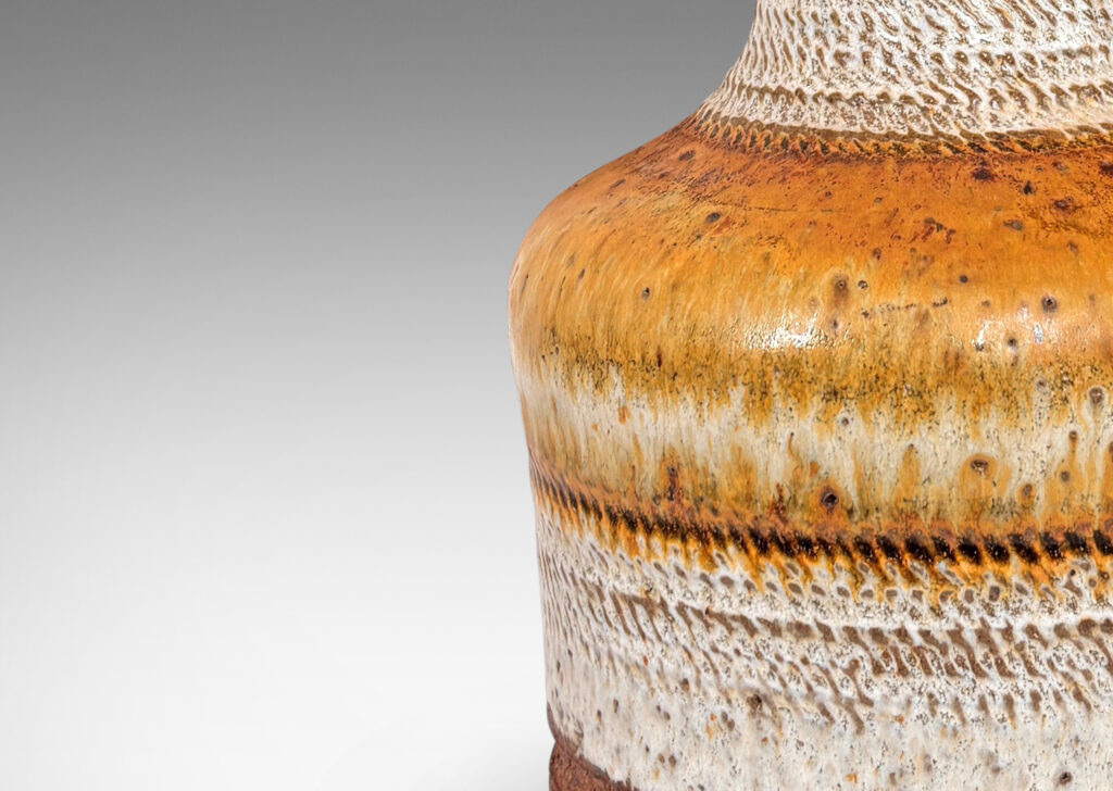 Gallery BAC modeled drum form with tall conical neck, with carved rope-like bands of diagonal hatches, and glazed in ivory and sandy tones