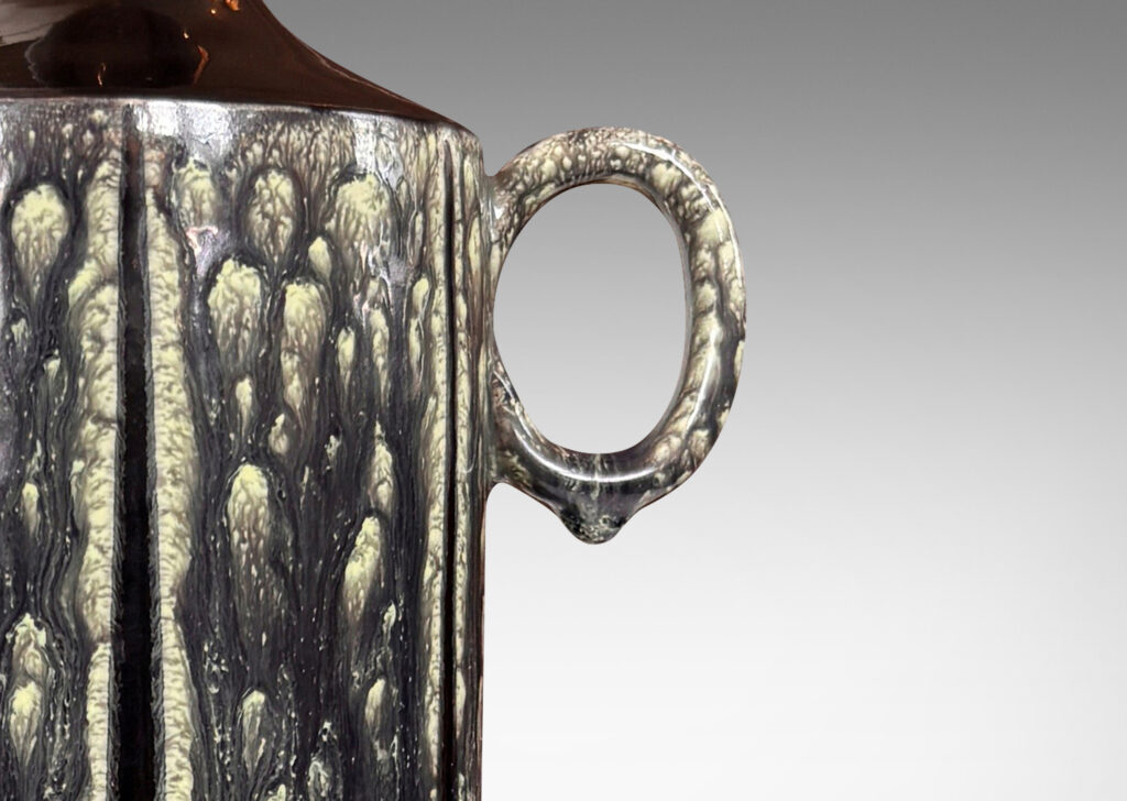 Gallery BAC cylindrical form, with ring handle and spouting mouth, glazed in flowing black-pale celadon