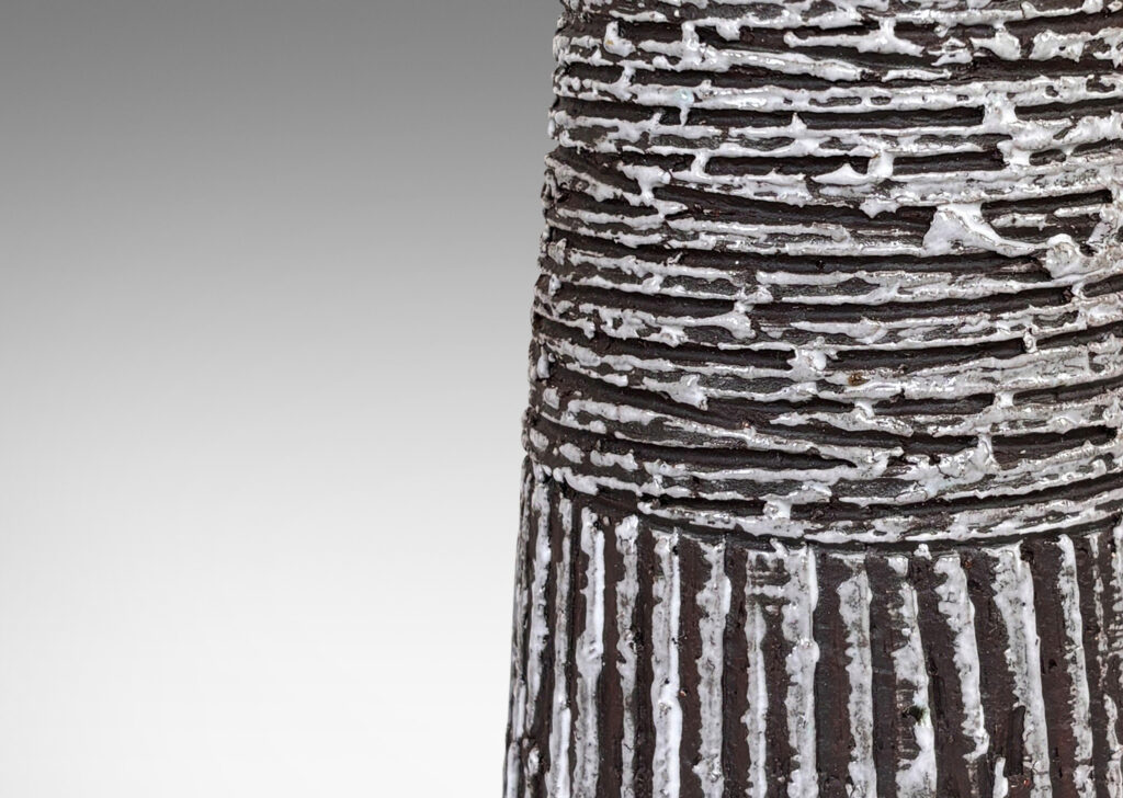 Gallery BAC upwardly tapered cylindrical form with carved horizontal and vertical ridges, glazed in matte brown with brushed gloss white accents