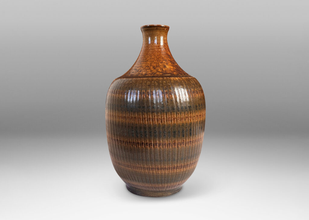 Gallery BAC tapered ovoid form with ribbed texture and spouting neck and mouth, glazed in a flowing dark brown