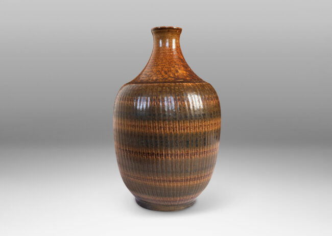 Gallery BAC tapered ovoid form with ribbed texture and spouting neck and mouth, glazed in a flowing dark brown