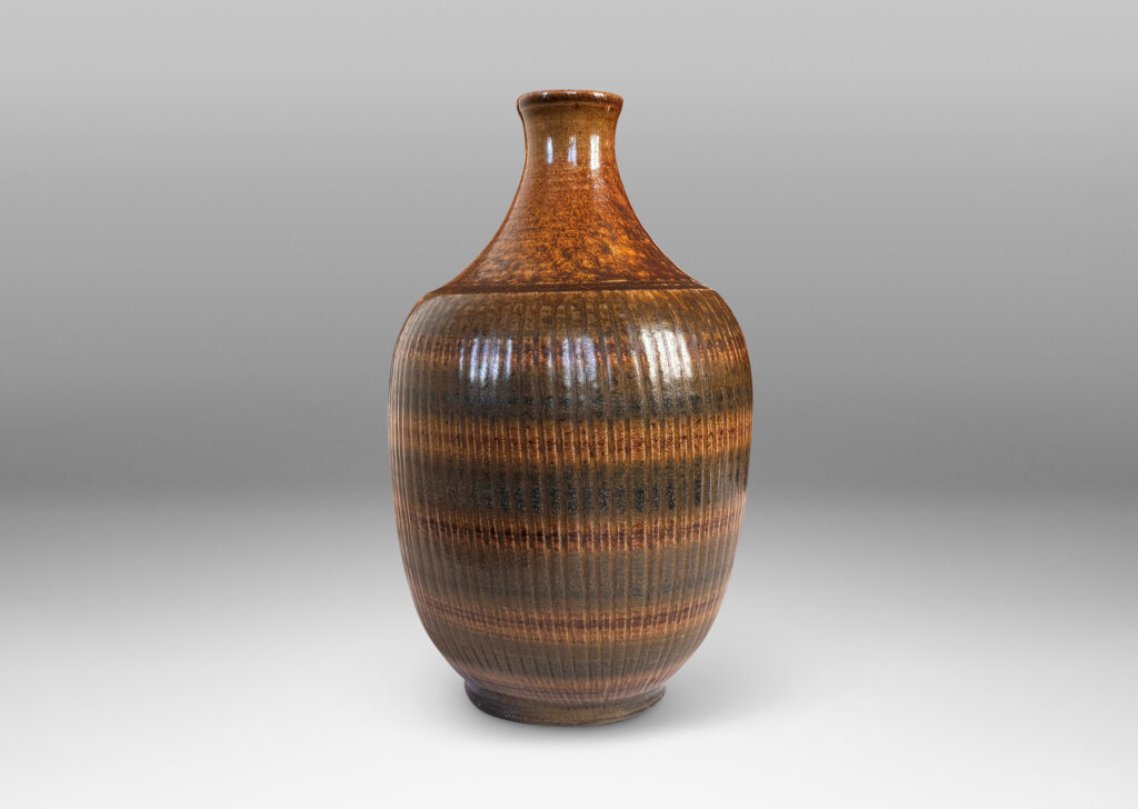 Gallery BAC tapered ovoid form with ribbed texture and spouting neck and mouth, glazed in a flowing dark brown