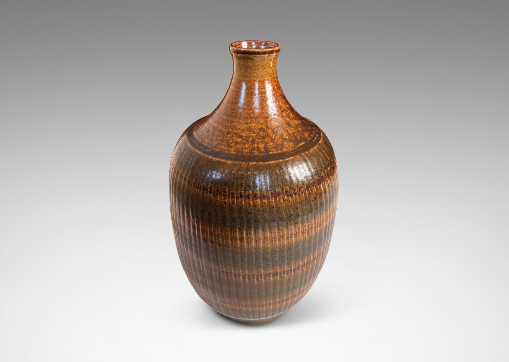 Gallery BAC tapered ovoid form with ribbed texture and spouting neck and mouth, glazed in a flowing dark brown