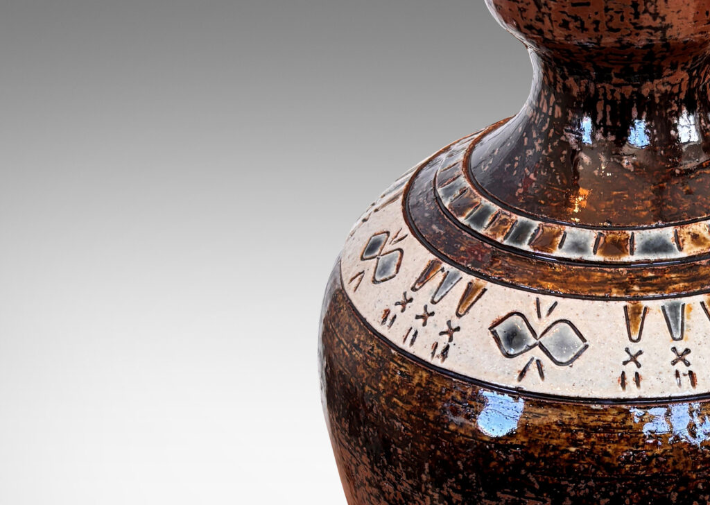 Gallery BAC urn style tapered ovoid form with textured surface with bands of carved geometric designs, glazed in brown, with ivory and gray-blue