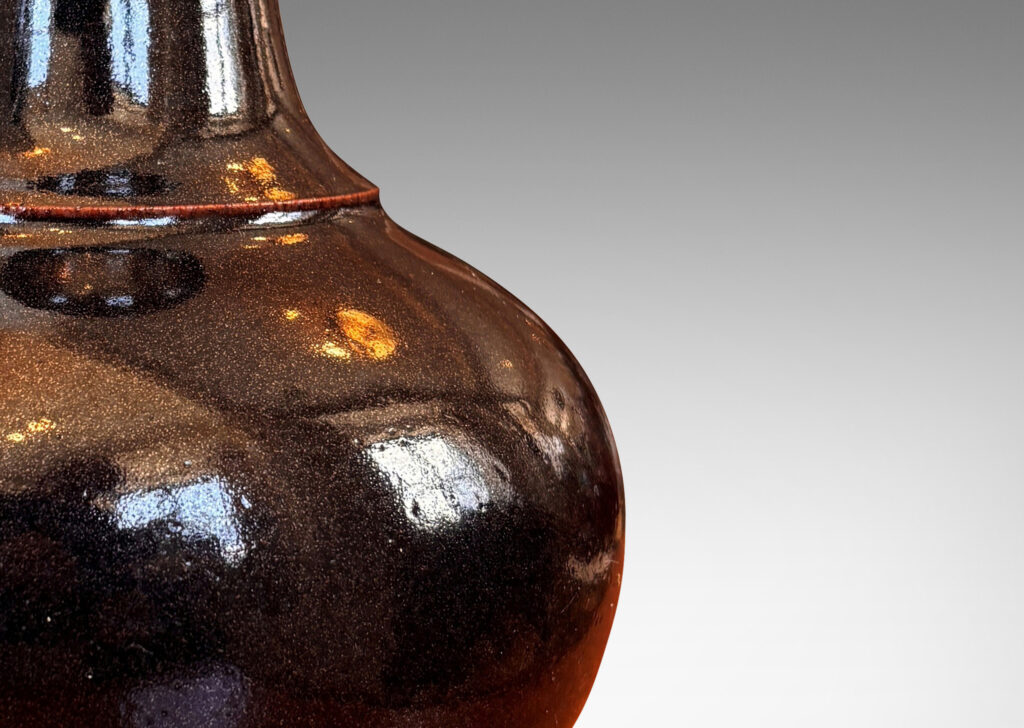 Gallery BAC compressed globe form with wide cove neck, glazed in shiny black with hints of oxblood red