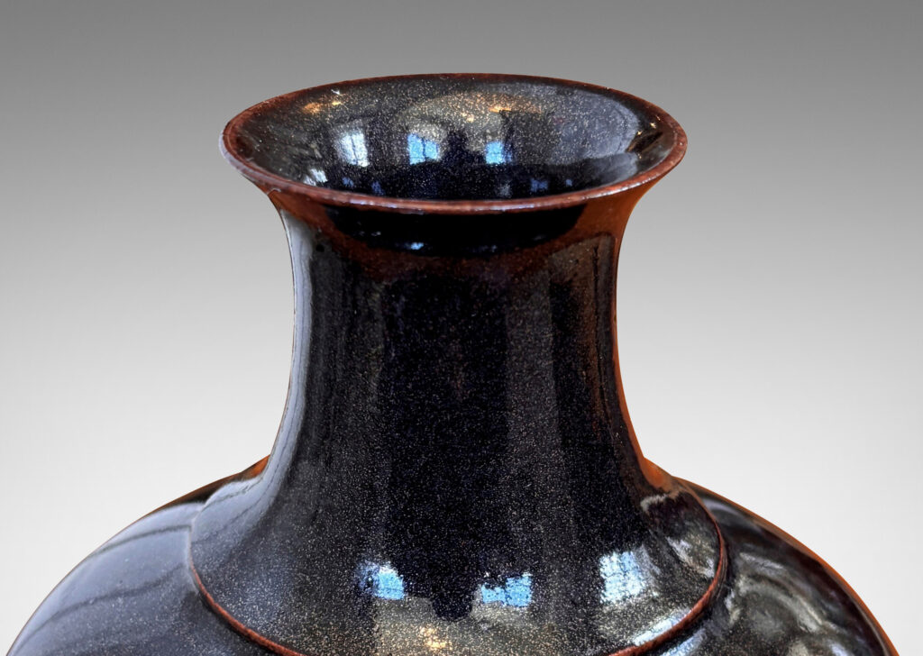 Gallery BAC compressed globe form with wide cove neck, glazed in shiny black with hints of oxblood red