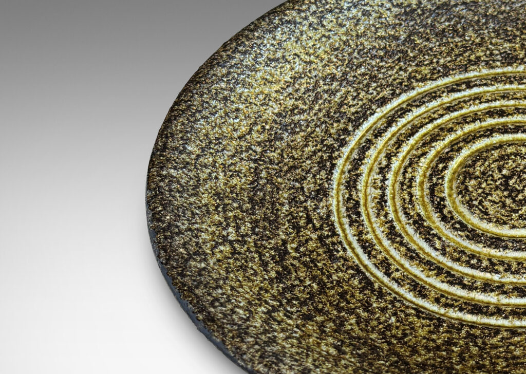 Gallery BAC shallow round form with a rustically textured and concentrically grooved interior glazed in black and green-gray, and a smooth exterior in gloss black
