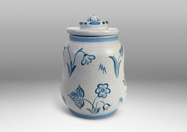 Gallery BAC undulating ovoid form with a disk lid with floral style finial, glazed in a pale gray craquel, with wildflower ornaments painted in blue
