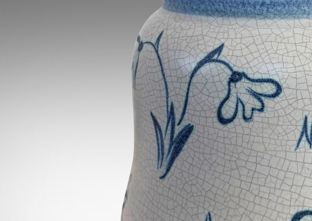 Gallery BAC undulating ovoid form with a disk lid with floral style finial, glazed in a pale gray craquel, with wildflower ornaments painted in blue