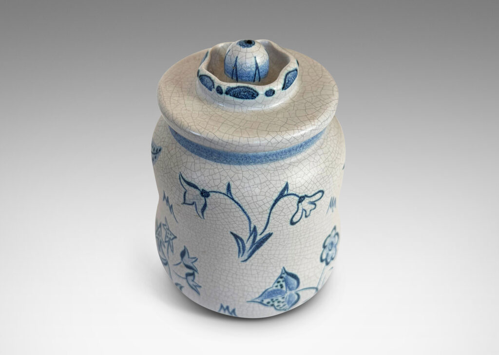 Gallery BAC undulating ovoid form with a disk lid with floral style finial, glazed in a pale gray craquel, with wildflower ornaments painted in blue