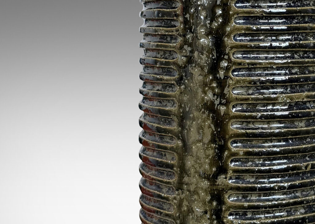 Gallery BAC cylindrical form with columns of carved lines and tall conical neck, glazed in a shiny dark mossy green