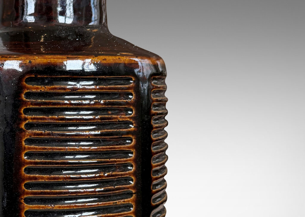Gallery BAC cylindrical form ornamented with columns of carved lines and a tall conical neck, glazed in a shiny brown glaze